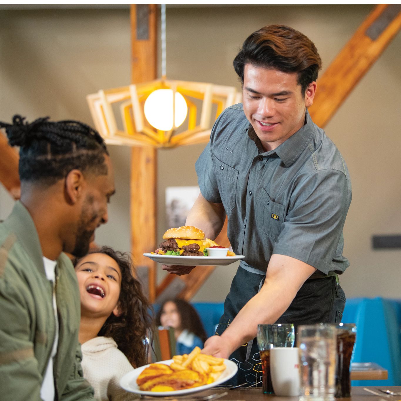 Male server placing food on a table with a father and child