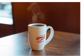 Mesa marrón con una taza de café de Denny's con el logotipo de Denny's y la frase "Es hora de ir a un Diner" en primer plano