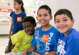 Image of 4 kids smiling and looking at the camera while wearing orange No Kid Hungry stickers. 