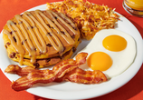 Stack of 2 pumpkin pecan pancakes, two bacon strips, two sunny side up eggs and a serving of hashbrowns on a plate. 