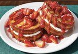 Image shows the NEW Strawberry Stuffed French Toast featuring Four slices of Brioche French Toast stuffed with sweet cream cheese filling and topped with strawberries, strawberry sauce and powdered sugar.