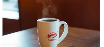 Brown table with Denny's coffee cup with Denny's logo on and "It's Diner Time" on the front 