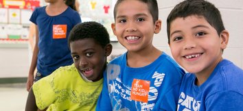 Image of 4 children smiling and looking at the camera, while wearing orange No Kid Hungry stickers.