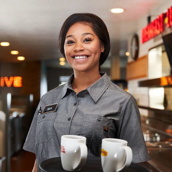 Un camarero sonriendo con una bandeja con tazas de café