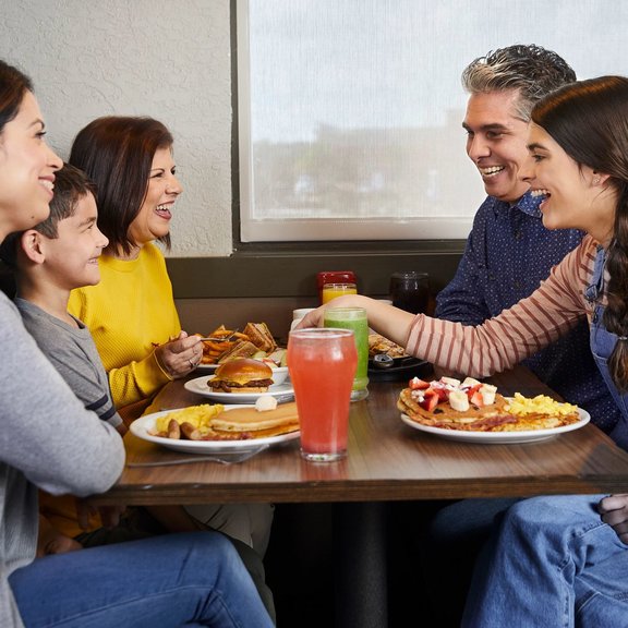 Family sitting in a booth enjoying a meal at Denny's. Family includes a mother, son, grandmother, father and daughter. 