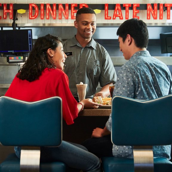 Two multicultural diners and a denny's server in the diner. 